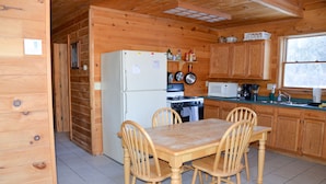Cocina de cabaña de madera con mesa y sillas, refrigerador, estufa, microondas y armarios de madera.
