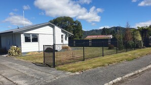 A residential house with a fenced yard, a satellite dish, and a small shed in the background. - Kiwiana Gem to enjoy in Reefton (Reefton)
