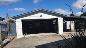 A single-story building with a garage entrance, a metal fence, and a small garden area with plants. - Kiwiana Gem to enjoy in Reefton (Reefton)