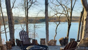 A fire pit area with Adirondack chairs and a view of a lake.