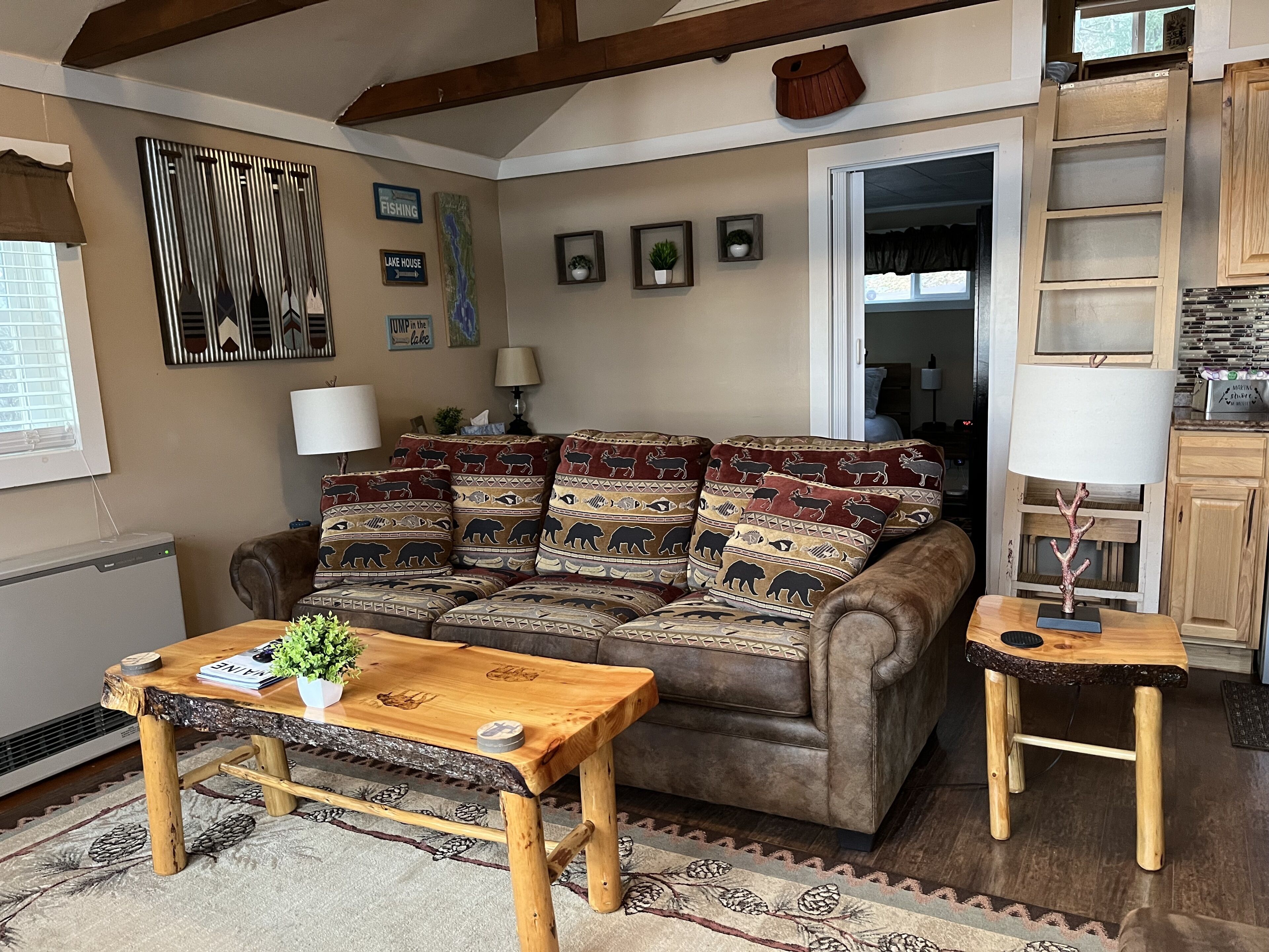 A cozy living room with a brown leather sofa adorned with patterned cushions, a wooden coffee table, and a small side table with a lamp.