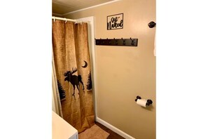 A bathroom with a brown shower curtain featuring a moose and crescent moon design, a towel rack with a 'First Naked' sign, and a toilet paper holder. - The Eagles Nest! ☀Four Seaon Lakeside Retreat☀ (Hudson)