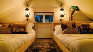 Un dormitorio acogedor en el ático con dos camas de madera, cada una con un cojín con motivos de ciervo, una ventana pequeña y dos faroles de pared.