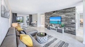 A modern living room with a grey sofa, a coffee table, and a flat-screen TV mounted on a textured wall. - Luxury condo on the beach  (Naples)