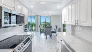 A modern kitchen with white cabinetry, a built-in oven, and a dining area with a table and chairs. - Luxury condo on the beach  (Naples)