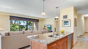 A modern kitchen with a granite countertop, wooden cabinets, and a built-in sink. - Kaanapali Alii 225 - Expansive 2BR Interior Corner Remodel w/ Partial Ocean Views! (Lahaina)