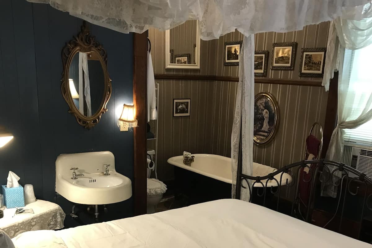 A hotel room with a large bed, a bathroom with a bathtub, a sink, and a mirror.