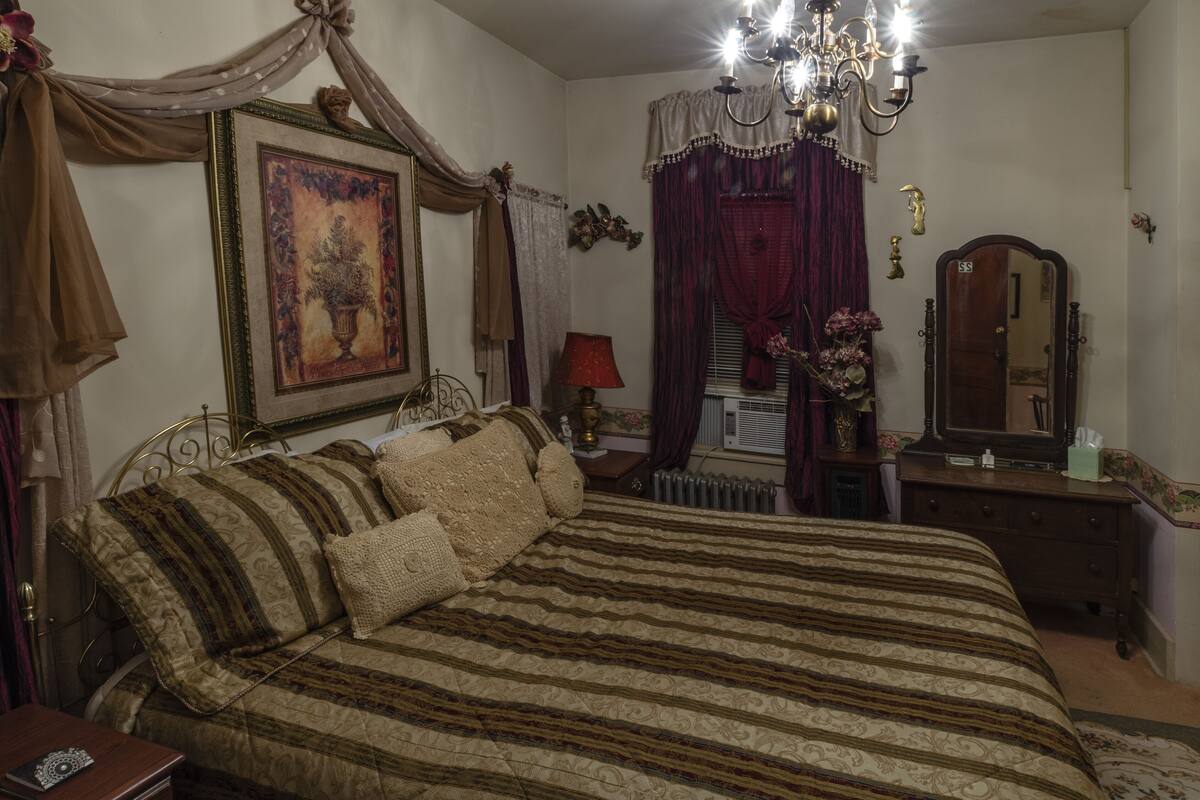 A bedroom with a large bed, a chandelier, a dresser, and a mirror.
