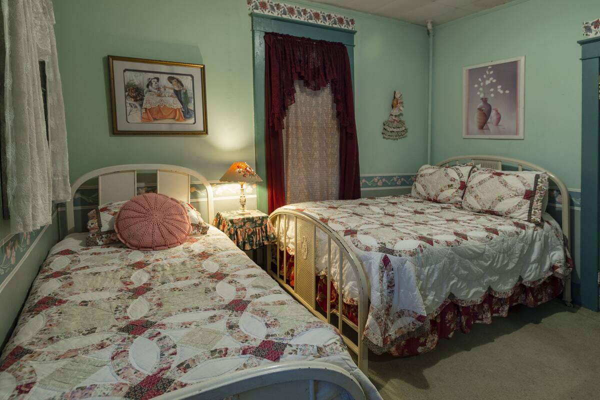 A room with two beds, a nightstand, a lamp, and a window with curtains.