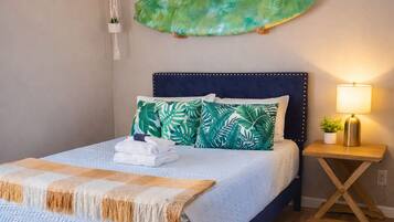 Un dormitorio con cama, mesita de noche, planta en la pared y ventilador de techo.