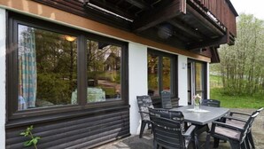 Uma área moderna para refeições ao ar livre com mesa, cadeiras, janelas amplas e um deck de madeira.