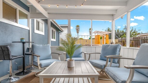 A covered patio with light blue cushioned chairs, a white table, and a potted plant. - Backyard Playset Family Getaway Home STR25-000025 (Marina)