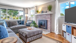 A modern living room with a fireplace, large windows, and a flat-screen TV. - Backyard Playset Family Getaway Home STR25-000025 (Marina)