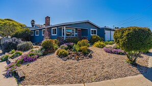 A two-story house with a blue exterior, a red door, and a well-maintained garden with various plants and flowers. - Backyard Playset Family Getaway Home STR25-000025 (Marina)