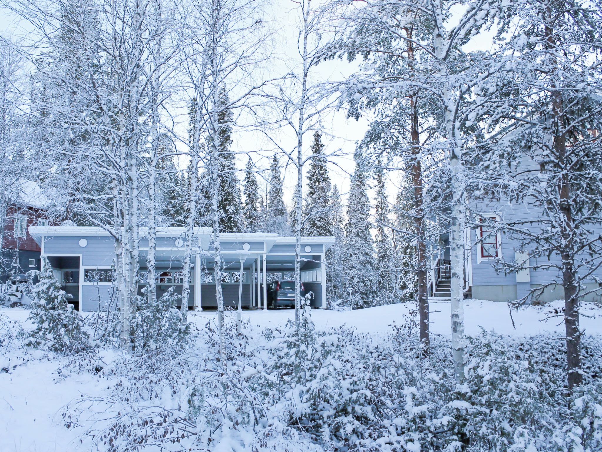 Lumipeitteinen rakennus, jossa on autotalli ja portaat, jotka johtavat sisäänkäynnille.