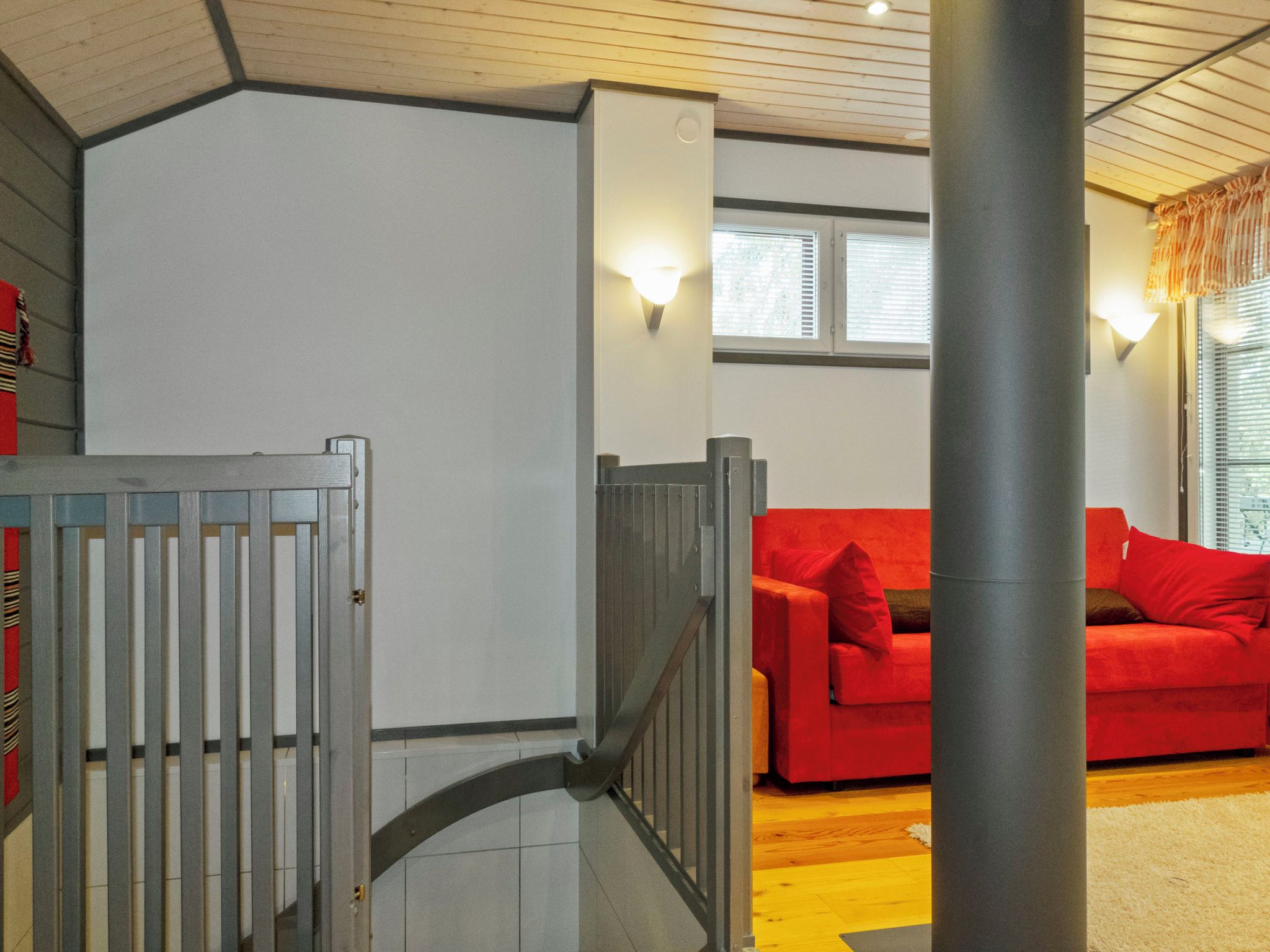 Un escalier avec une rampe en métal menant à une pièce où se trouve un canapé rouge et une fenêtre avec des stores.