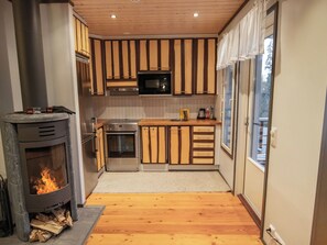 A modern kitchen with a wood-burning stove, stainless steel appliances, and wooden cabinetry.