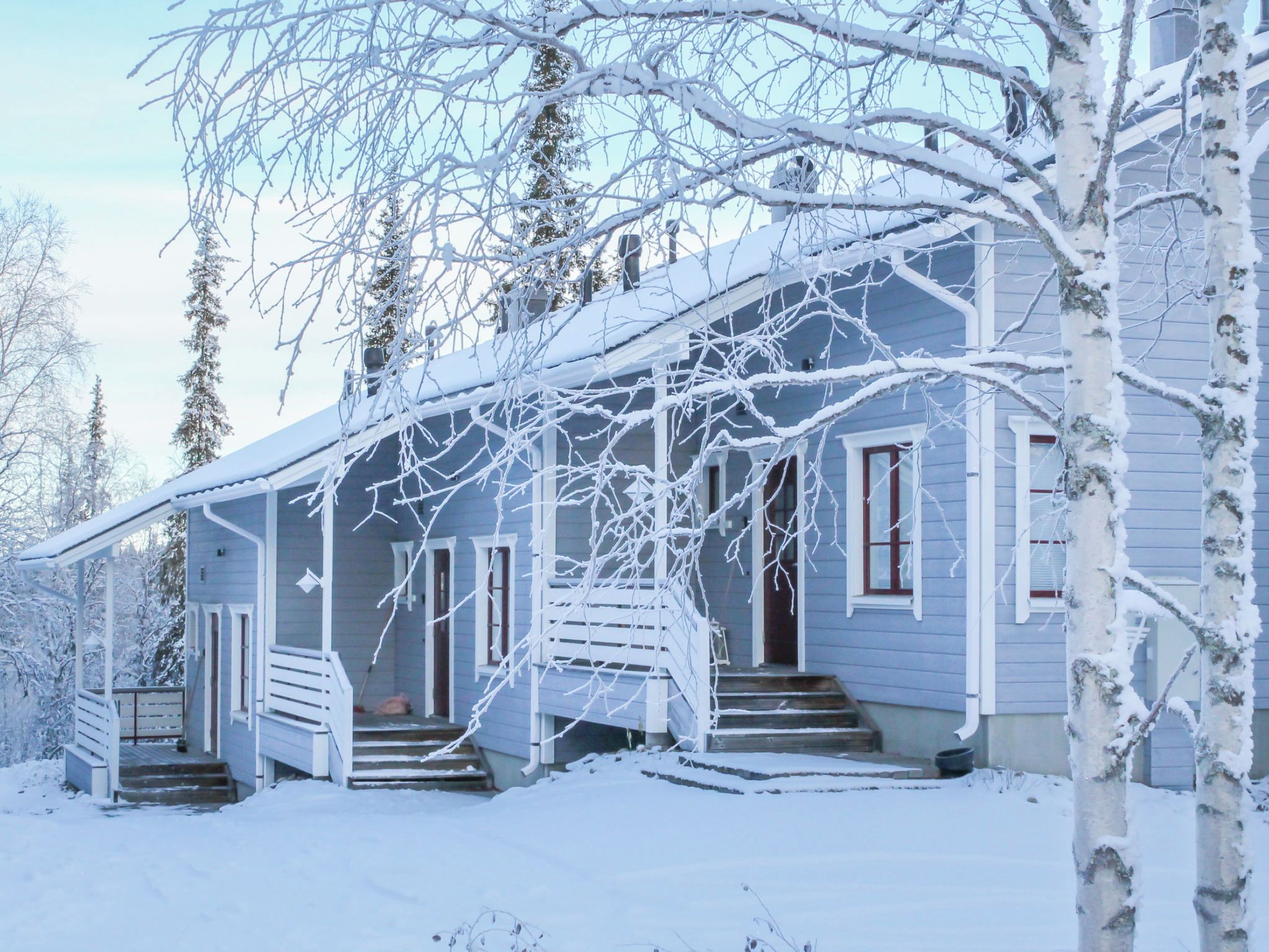Ein mit Schnee bedecktes Haus mit einer Veranda und Treppen zum Eingang.