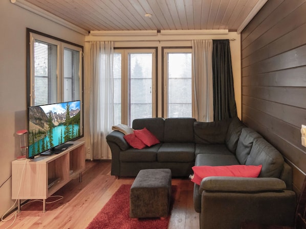 A modern living room with a sectional sofa, a flat-screen TV, and a wooden floor.