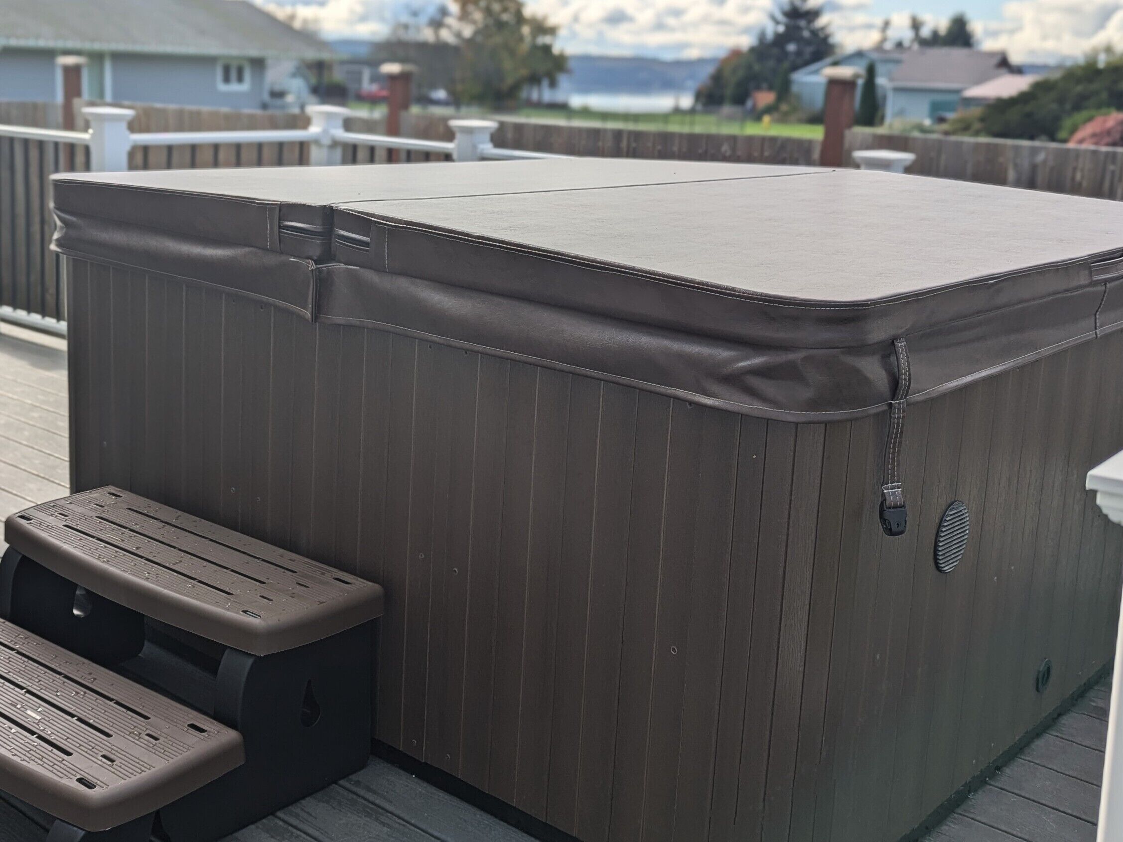 A hot tub with a bench, surrounded by a wooden deck and a view of the ocean.
