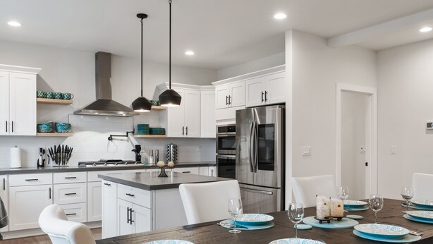 A modern kitchen with white cabinets, stainless steel appliances, and a wooden dining table set with blue plates and glasses. - 5BR vacation home Hot Tub/Game Room/Water Views/BBQ/firepit/LG Yard (Camano)