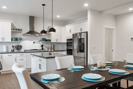 A modern kitchen with white cabinets, stainless steel appliances, and a wooden dining table set with blue plates and glasses.