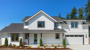 A two-story house with a front porch, a garage, and a well-maintained front yard with various plants. - 5BR vacation home Hot Tub/Game Room/Water Views/BBQ/firepit/LG Yard (Camano)