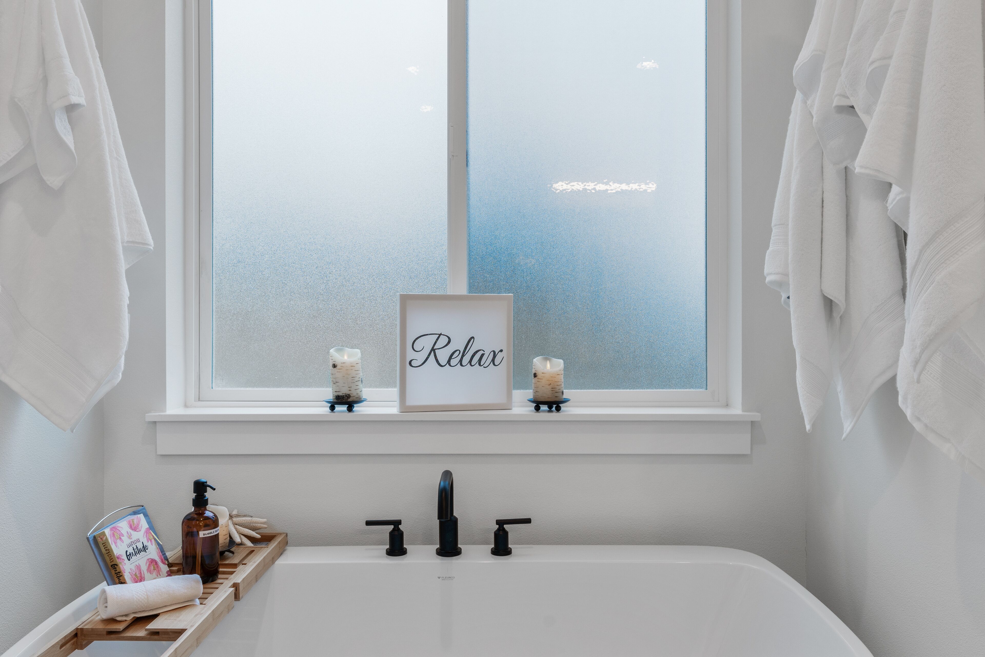 Un baño con bañera, una ventana con vidrio esmerilado y un cartel que dice 'Relax'.