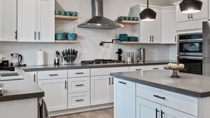 A modern kitchen with white cabinets, stainless steel appliances, and pendant lighting. - 5BR vacation home Hot Tub/Game Room/Water Views/BBQ/firepit/LG Yard (Camano)