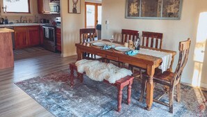 A dining area with a wooden table set for two, a kitchen in the background, and a decorative banner on the wall. - Red rock views ♦ Private access to the forestry ♦ The perfect romantic escape (Sedona)