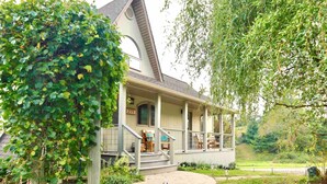 A two-story house with a covered porch, a stone pathway leading to the entrance, and a well-maintained garden. - Dog-Friendly Cottage w/ Creek, Barn, Game Room, Fire Pit, Hot Tub, Sleeps 10 (Hillsville)