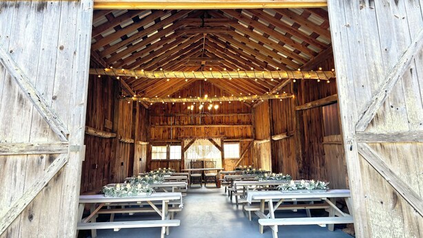 A rustic barn interior with wooden walls, a high ceiling, and string lights. Tables are set up for dining. - Dog-Friendly Cottage w/ Creek, Barn, Game Room, Fire Pit, Hot Tub, Sleeps 10 (Hillsville)