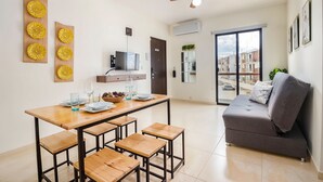 A modern living room with a grey sofa, wooden dining table with benches, a ceiling fan, and a view of buildings through a glass door. - Bright & Relaxing Full Apartment (Cancun)