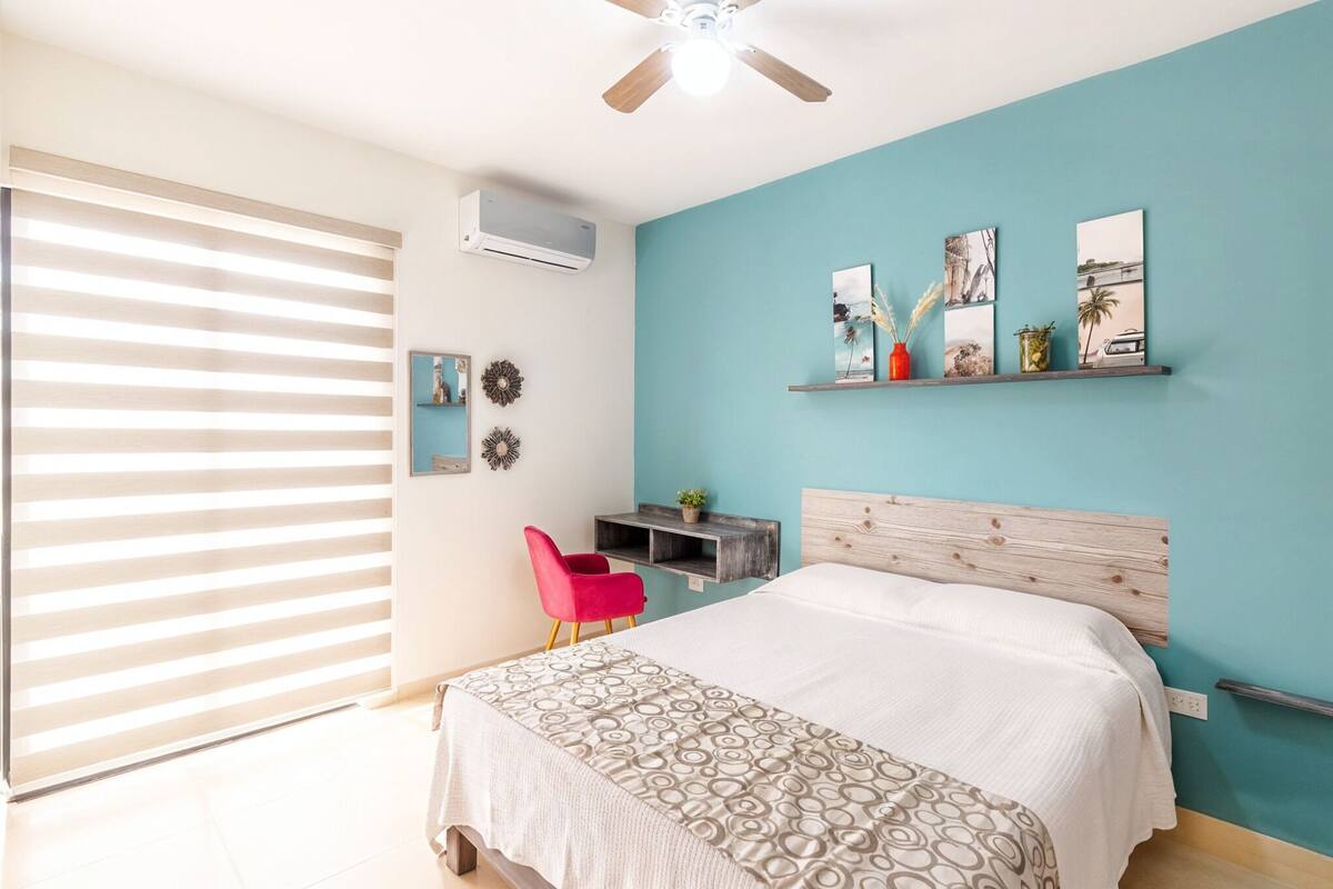 Quarto com uma cama, escrivaninha, cadeira e prateleira com quadros.
