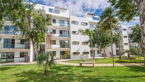 A modern multi-story building with balconies, surrounded by well-maintained grass and palm trees. - Bright & Relaxing Full Apartment (Cancun)