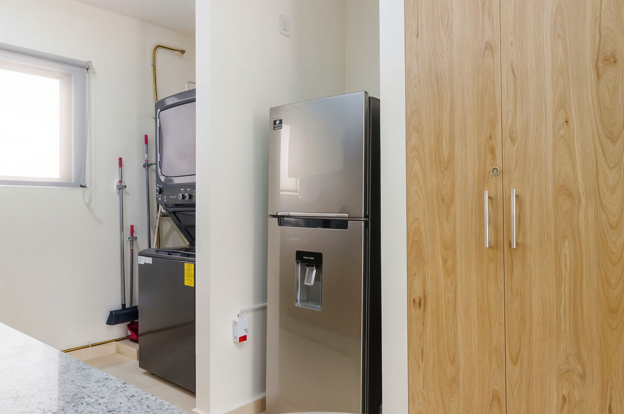 A kitchen with a stainless steel refrigerator, a water dispenser, and a window with blinds.