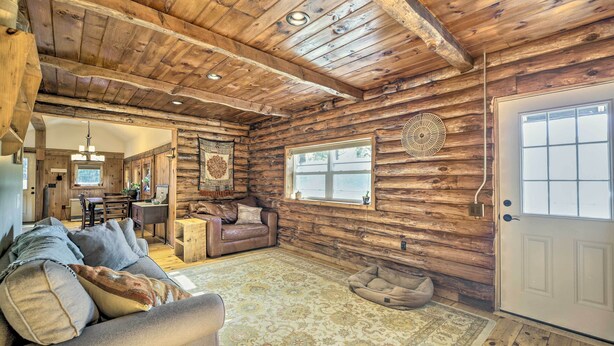 Interior de una cabaña de madera con techo de madera, un sofá con cojines, una alfombra, una cama para perro y una puerta.