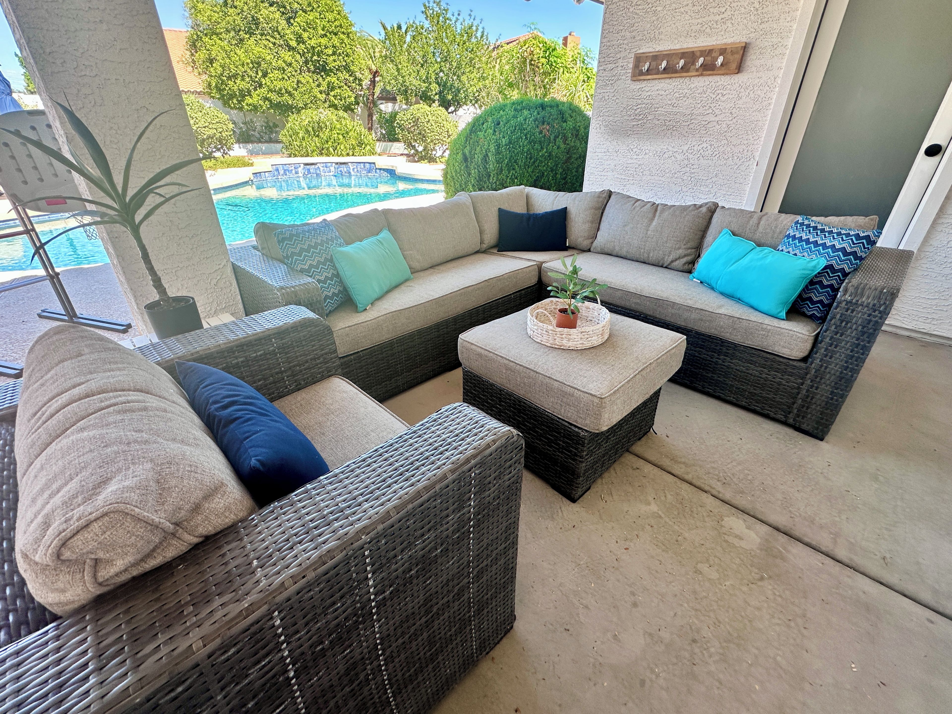 A sunlit outdoor seating area with wicker furniture, a small table with a plant, and a view of a swimming pool.