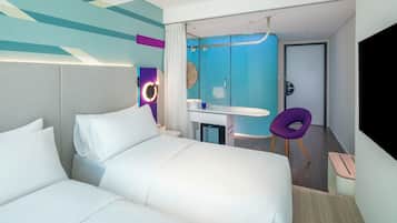 A modern hotel room with a bed, a desk with a chair, a bathroom, and a TV.