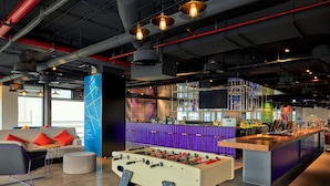 A modern bar area with a foosball table, bar stools, and a large screen. - Tru by Hilton Bac Giang City Centre (Bac Giang)