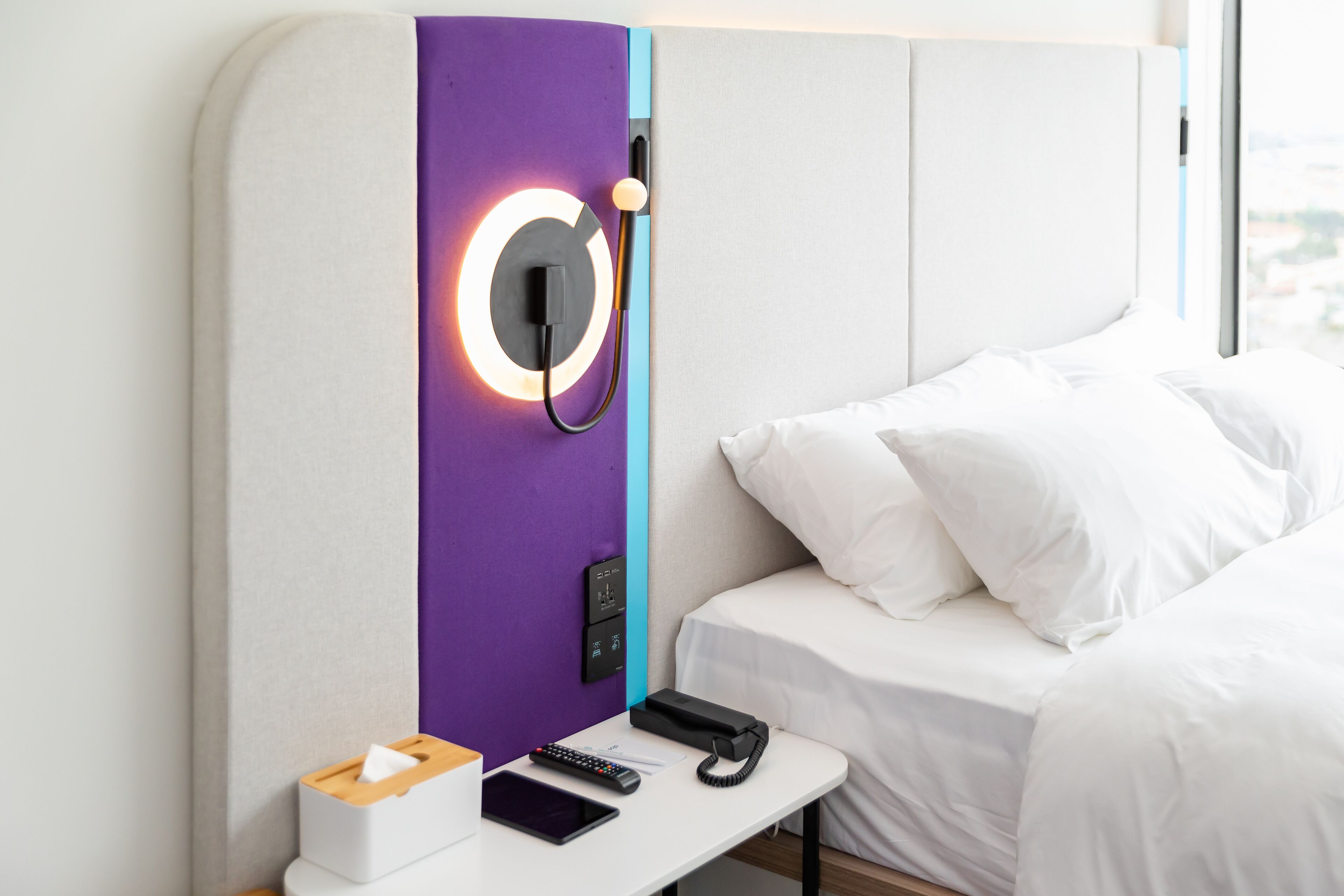 A hotel room with a bed, a bedside table with a phone, a remote control, and a tissue box.