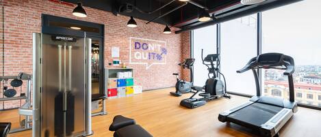 Un gimnasio con pared de ladrillo, cinta de correr, bicicletas estáticas y máquina de pesas.
