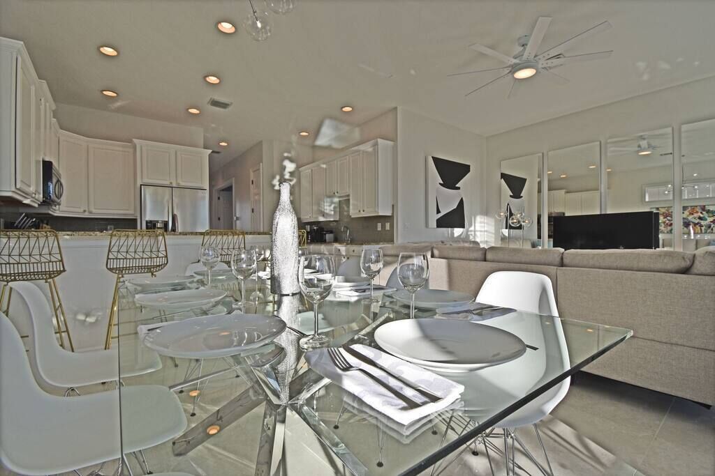 A modern dining area with a glass table, white chairs, and a chandelier.