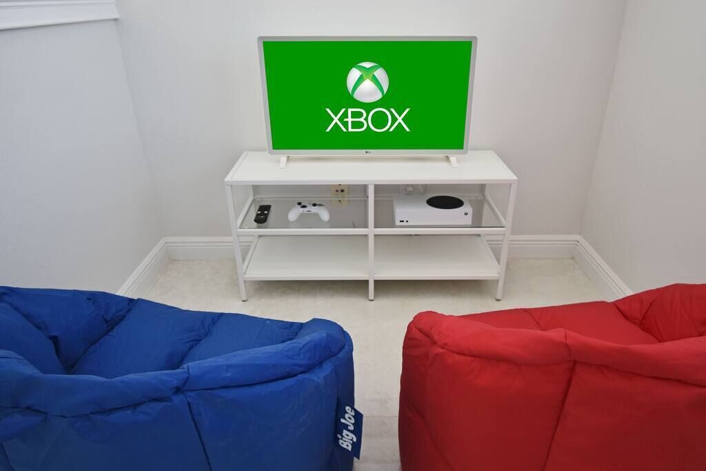 A room with a white entertainment unit displaying an Xbox logo, a blue bean bag chair, and a red bean bag chair.