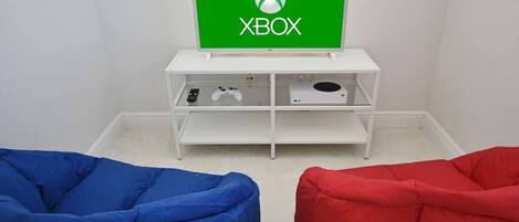 A room with a white entertainment unit displaying an Xbox logo, a blue bean bag chair, and a red bean bag chair.
