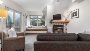 A modern living room with a fireplace, a sofa, a chair, and a window seat. - 1BR | Lake Placid Lodge | Steps to Creekside Gondola | Shared Pool, Hot Tub, & Lounge (Whistler)