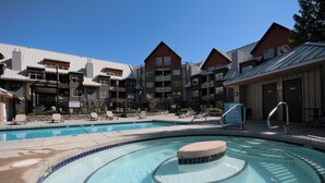 A swimming pool with lounge chairs and a hot tub area, surrounded by multi-story buildings with balconies. - 1BR | Lake Placid Lodge | Steps to Creekside Gondola | Shared Pool, Hot Tub, & Lounge (Whistler)