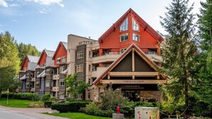A lodge with a prominent red and brown facade, multiple balconies, and a stone entrance. - 1BR | Lake Placid Lodge | Steps to Creekside Gondola | Shared Pool, Hot Tub, & Lounge (Whistler)