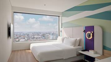 Una habitación de hotel moderna con un ventanal grande, una cama, una mesita de noche y un televisor montado en la pared.