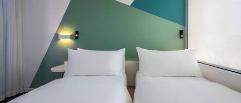 Habitación de hotel con dos camas, una mesita redonda pequeña y una lámpara fijada a la pared.
